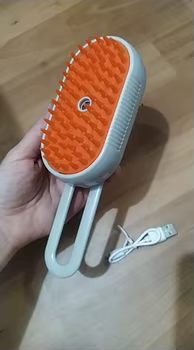 Customer photo: a hand holding the orange-bristle Groomty brush with its USB cable
